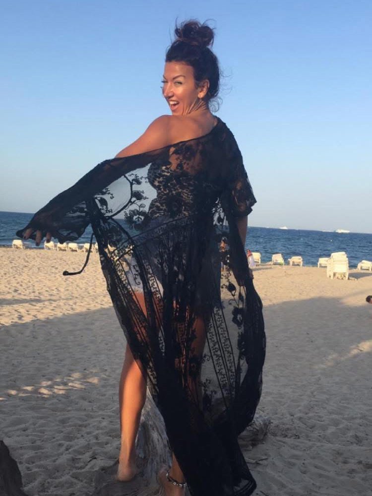 Jessica en una playa de Ibiza al atardecer, riendo y mirando por encima del hombro, con un caftán de encaje negro que se levanta con la brisa