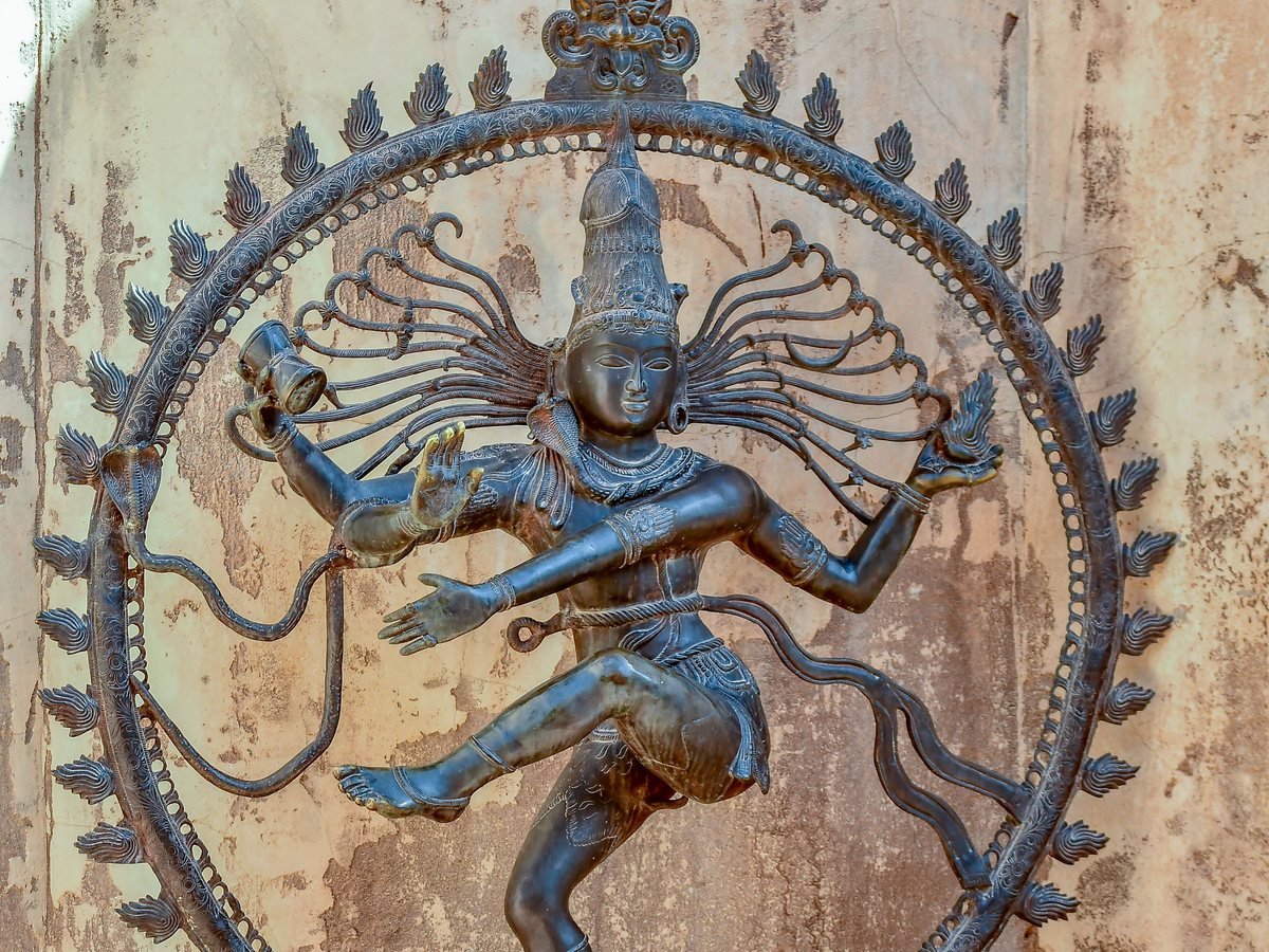 Un Shiva Nataraja de bronce, el Shiva danzante dentro de un círculo de llamas, ante una pared de yeso desgastada