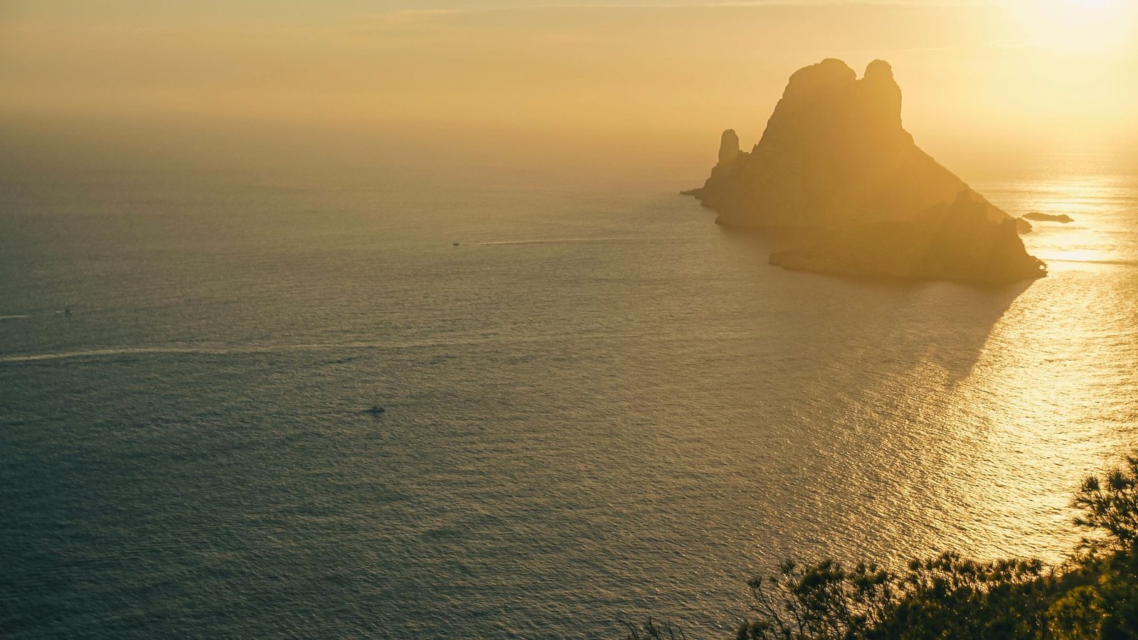 Es Vedrà alzándose sobre un mar dorado por el sol bajo, visto desde los acantilados de Ibiza