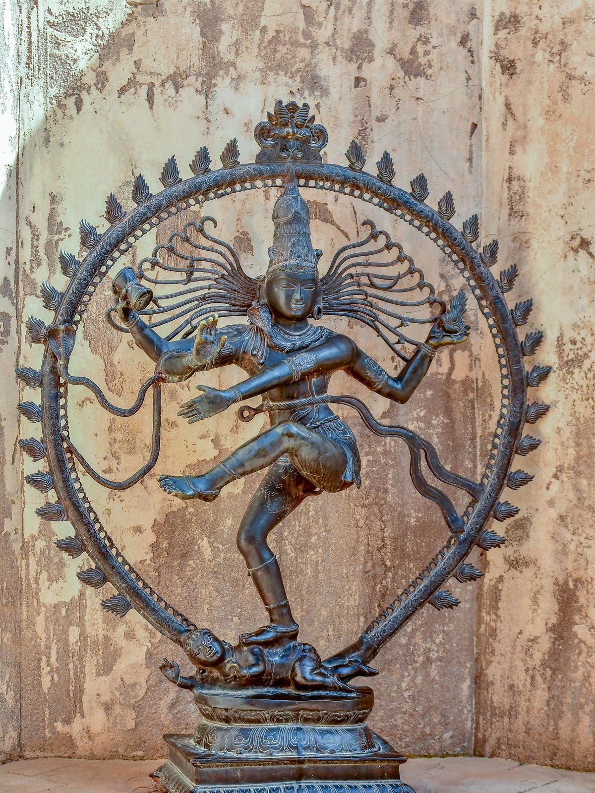 Un Shiva Nataraja de bronce, el Shiva danzante dentro de un círculo de llamas, ante una pared de yeso desgastada