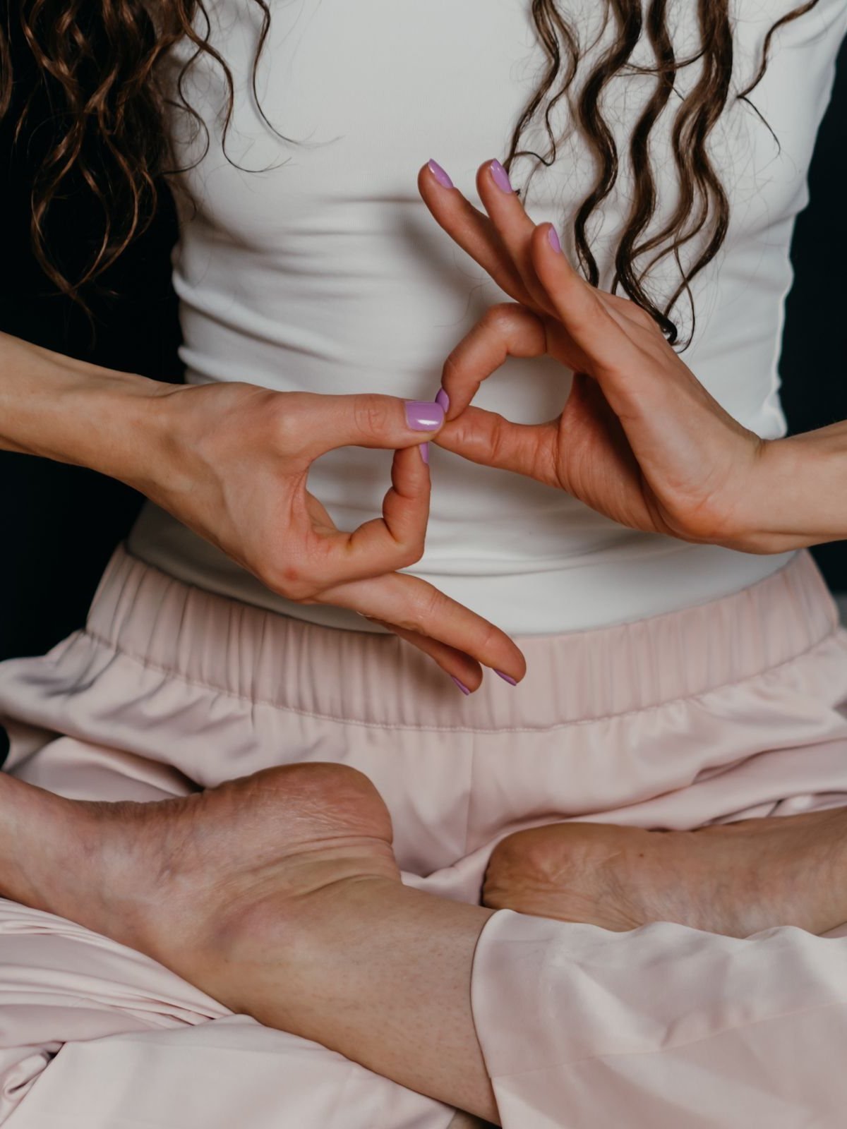 A woman seated cross-legged in white, her hands joined in a mudra at the heart